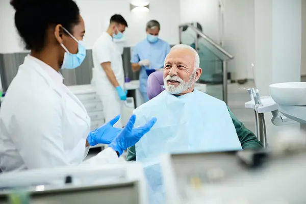 Older patient sitting in a dental chair calmly discussing oral health with the dentist.
