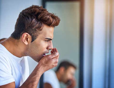 Man checking his bad breath by cusping his hand in front of his mouth