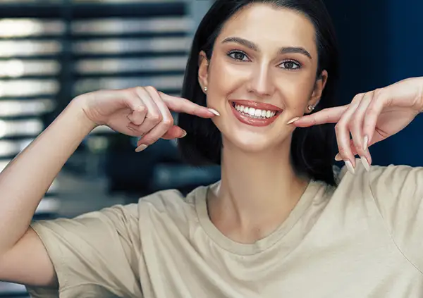 A woman smiling confidently while pointing to her bright white teeth, highlighting the results of a cosmetic dental procedure.