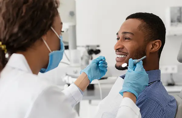 A dentist performing a dental check-up on a smiling male patient in a clinic, emphasizing professional care and comfort.