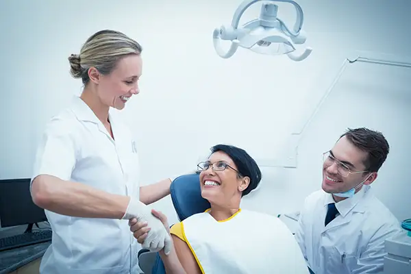 A woman smiling and shaking hands with her dentist and a dental hygienist during her first visit.