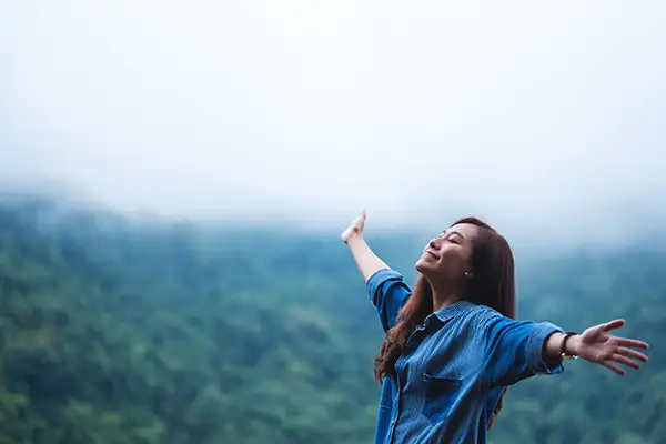 Smiling woman with arms outstretched in nature, emphasizing the holistic benefits of maintaining oral and overall health.