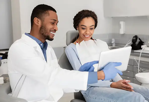 A smiling dental assistant presents DNA testing results a content patient seated in a dental chair.