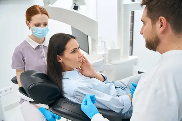 A dentist and assistant examining a female patient in a clinic, assessing symptoms of TMJ disorder.